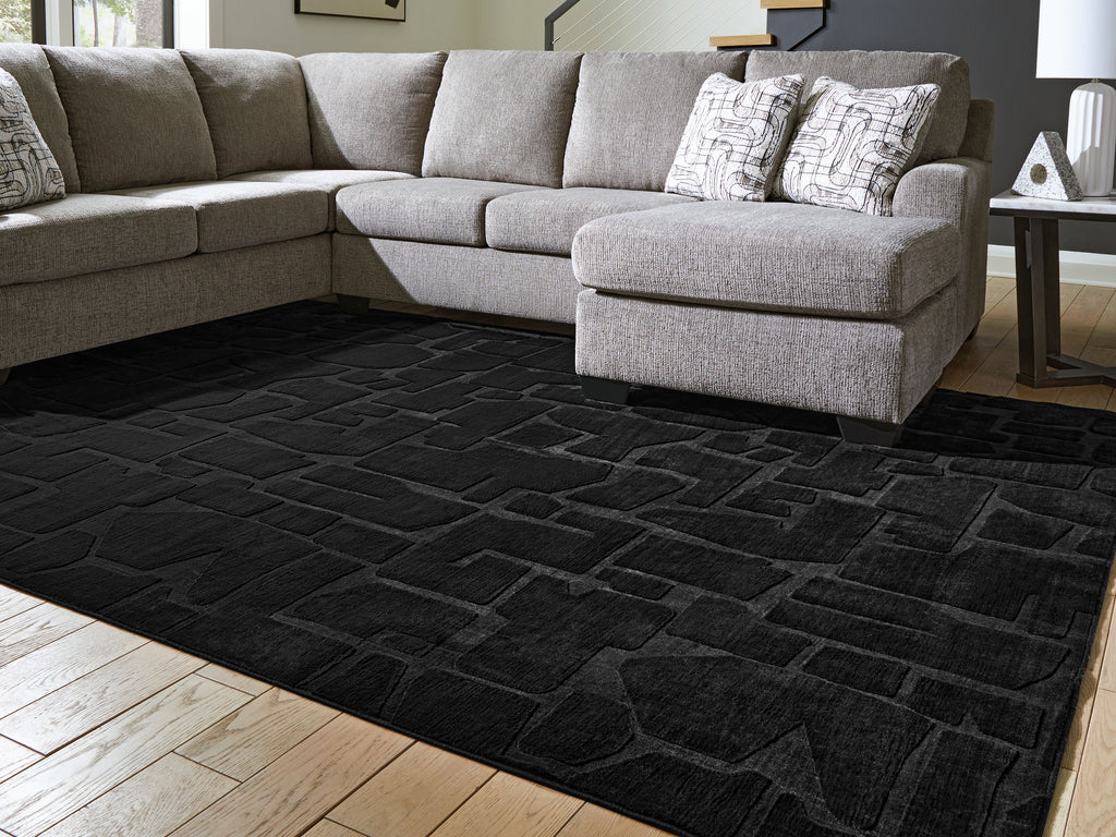 Washable rug, black brick-pattern design on hardwood floor, corner visible
