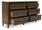 Brown dresser showing six drawers, long pulls, and carved trim with turned legs