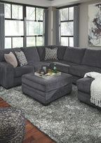 Slate gray upholstered ottoman with cushioned seat and dark legs in living room