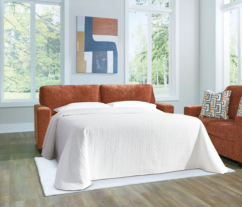 Sofa sleeper converted to a bed with white bedding and two patterned pillows.