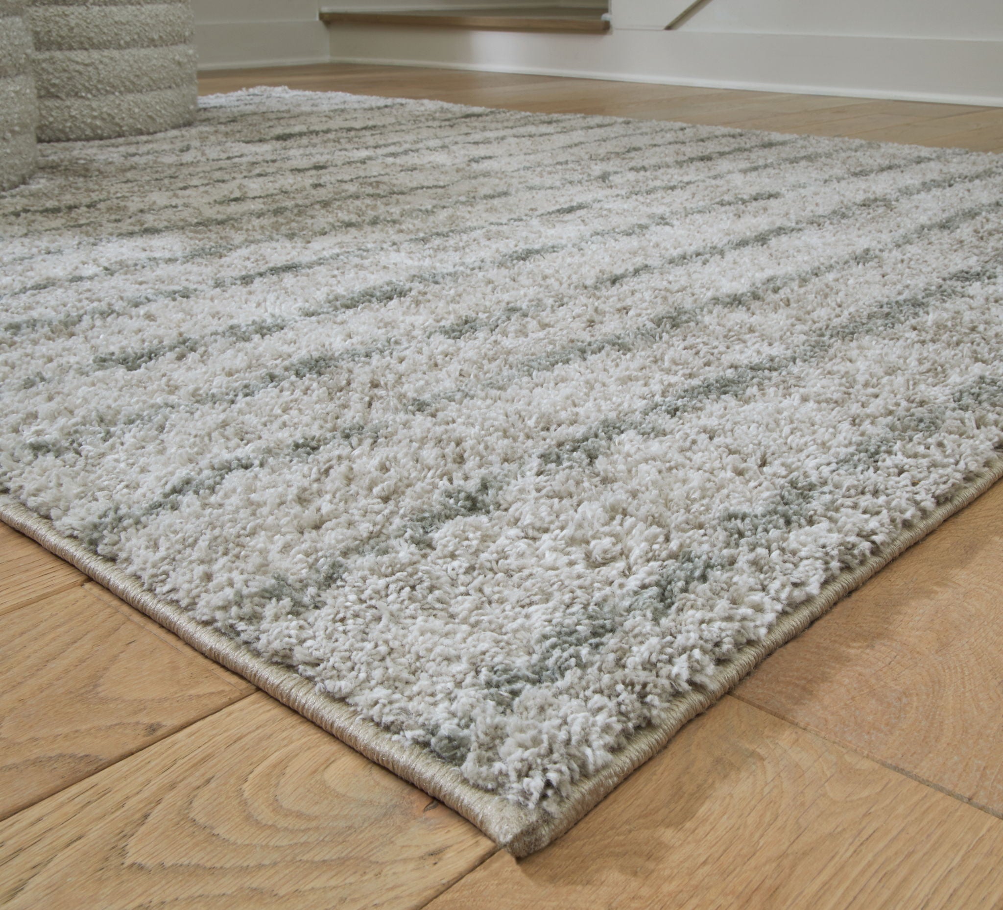 Cream and green rug corner with dense textured pile and flat stitched edge