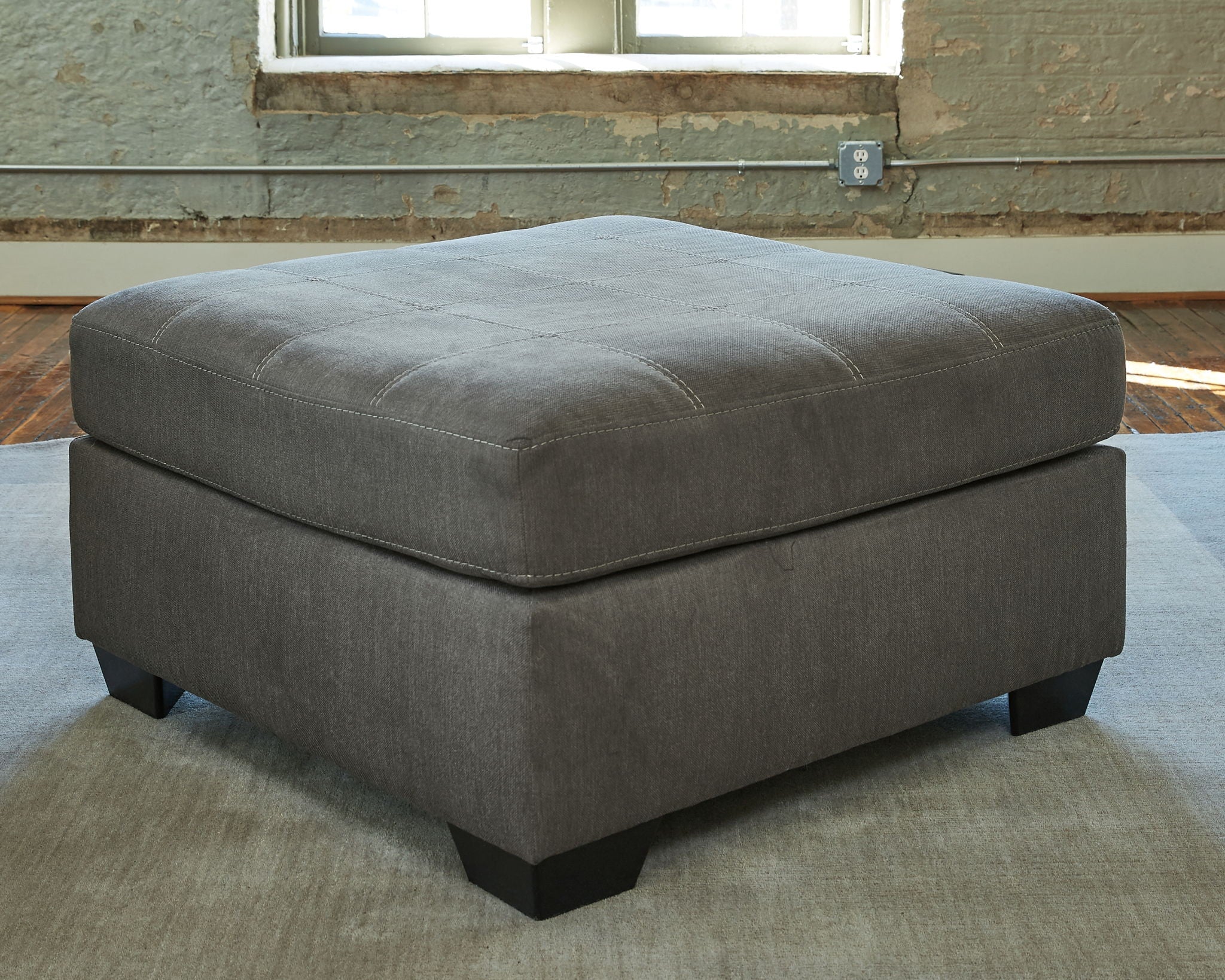 Gray square ottoman with padded seat, subtle tufting, and block feet
