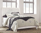 Whitewash queen panel headboard with upholstered white bed and patterned bedding