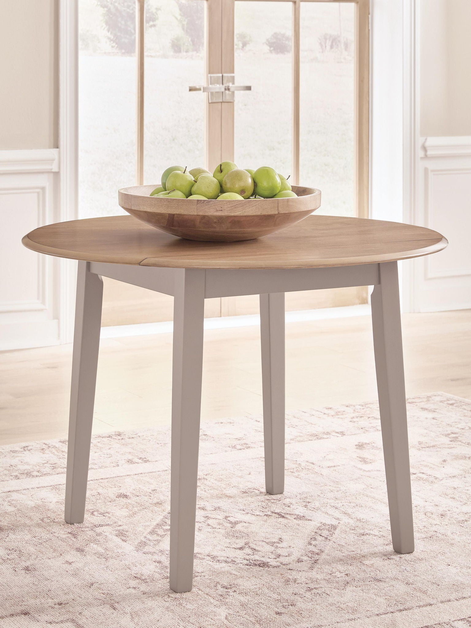 Round drop-leaf dining table with natural wood top and gray legs, leaves up