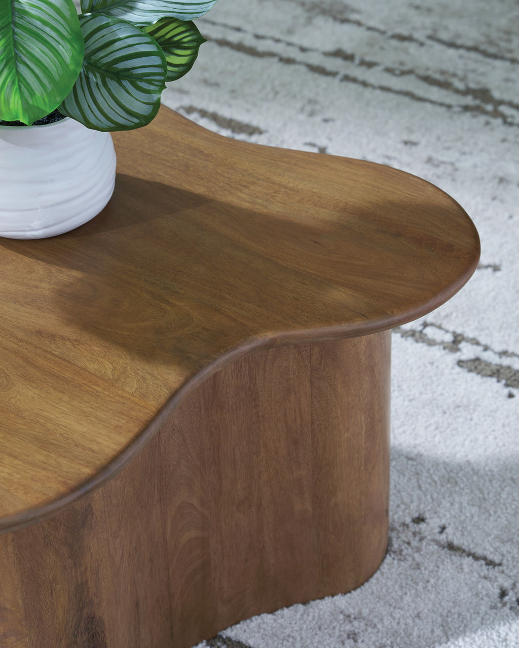 Brown accent cocktail table with oval-like rounded top and carved curved base
