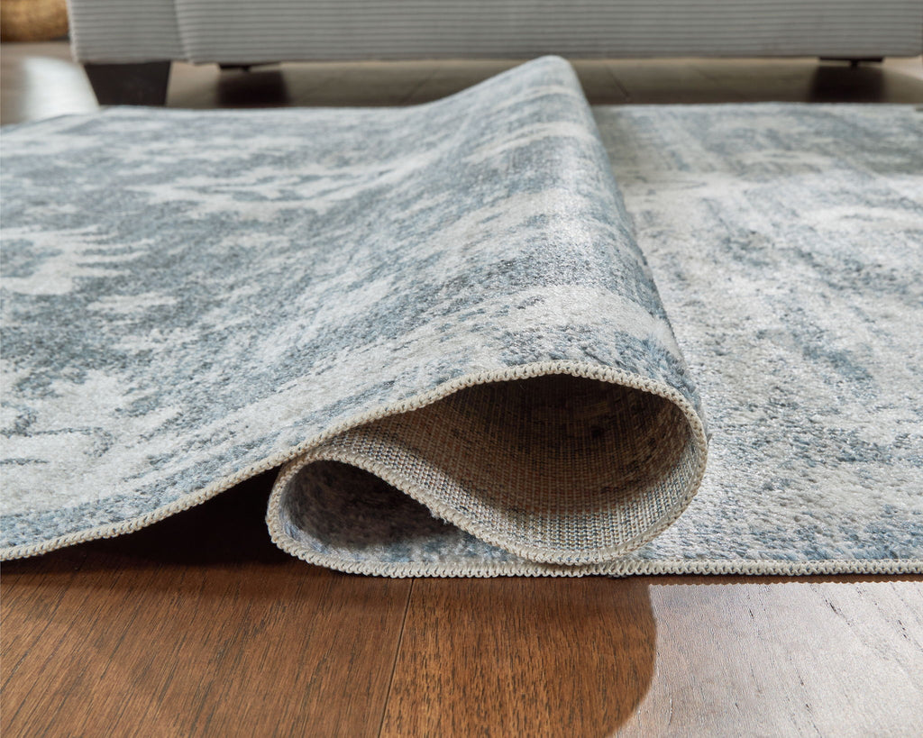 Rolled section of gray washable rug showing underside and distressed floral print