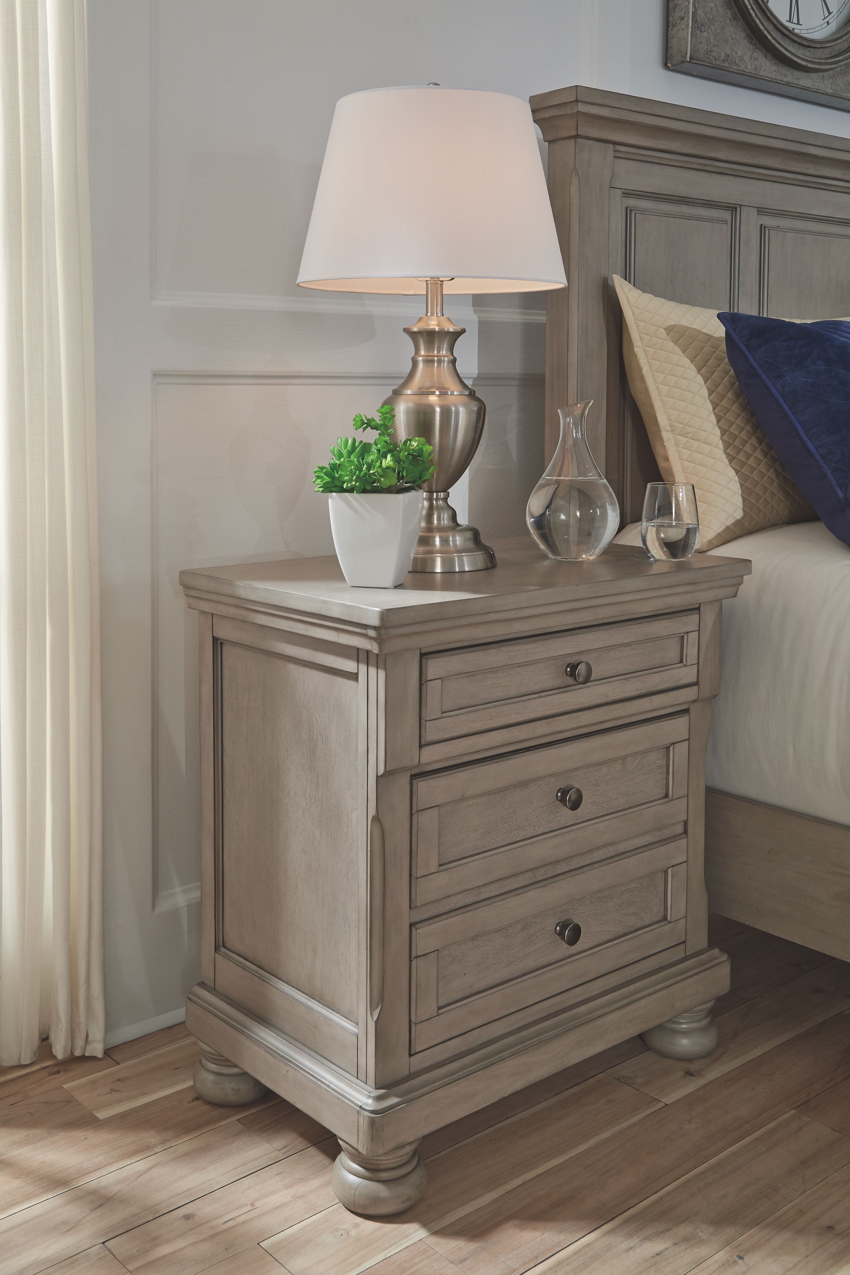Lettner night stand with three drawers and lamp on top, light gray finish.