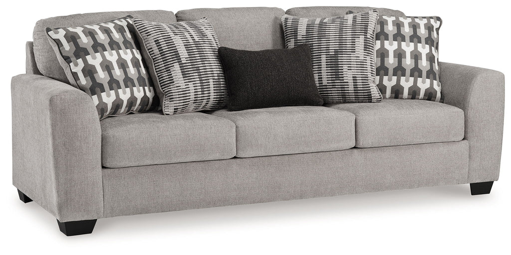 Gray upholstered loveseat with three patterned pillows and dark accent pillow