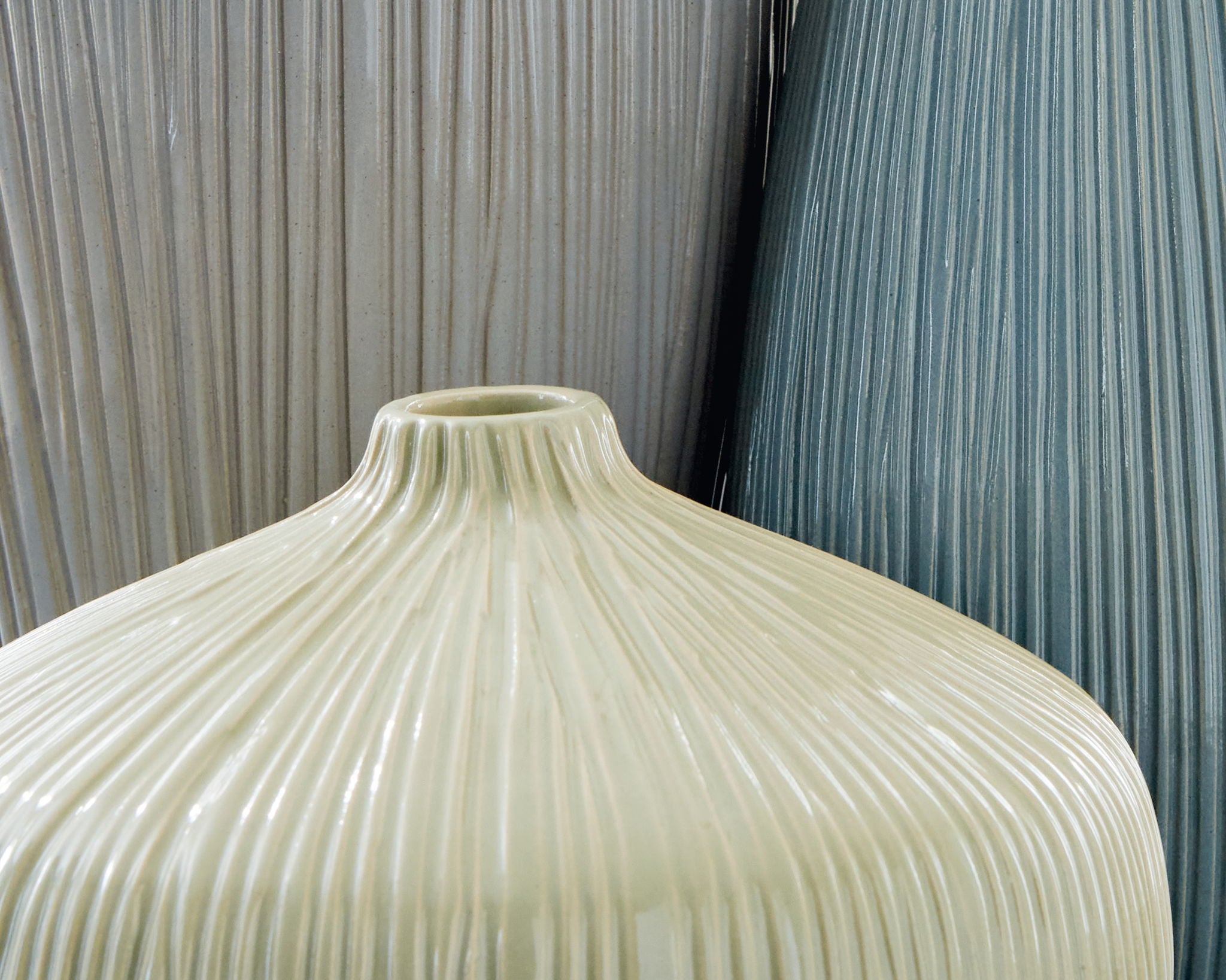 Ribbed ceramic vase in ivory with fluted texture, close-up of neck