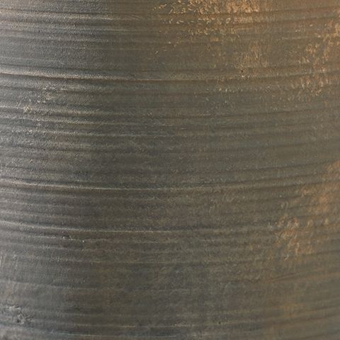 Close-up of antique gray vase surface with fine horizontal ridges and speckled metal finish
