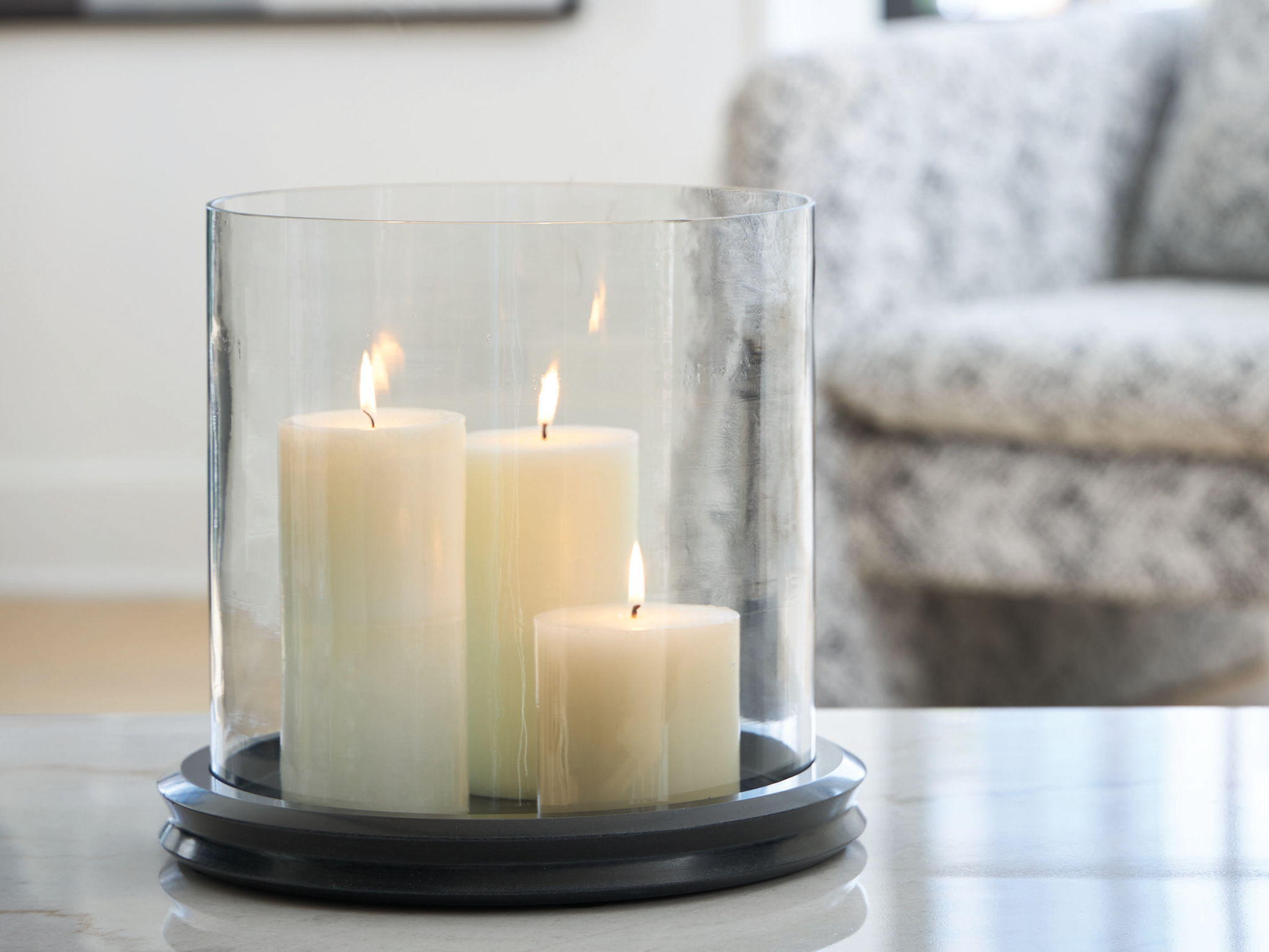 Glass cylinder candle holder with dark base, holding four lit white candles