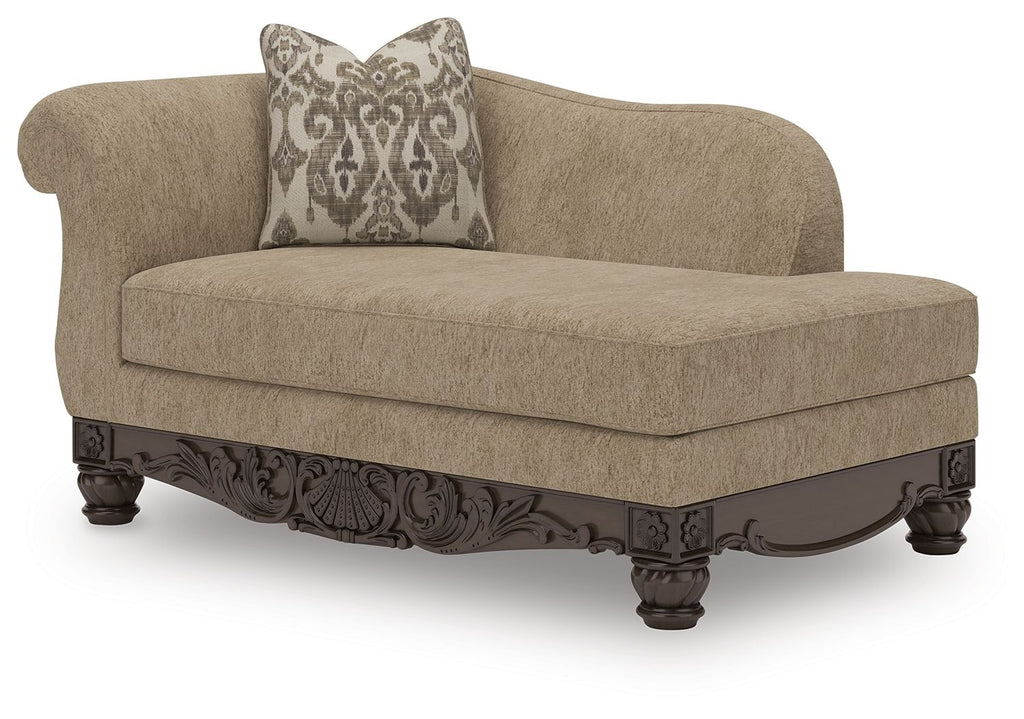 Beige corner chaise with patterned pillow and dark carved wooden base, angled view.