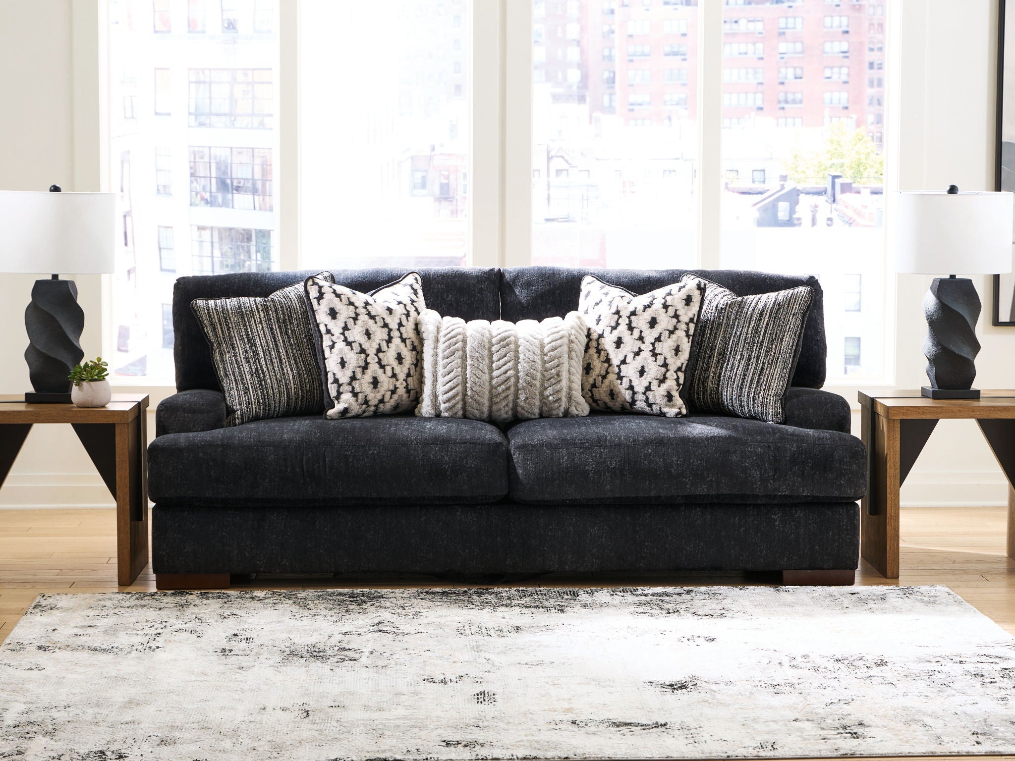 Black fabric sofa with three patterned pillows, two gray striped cushions, and wooden feet