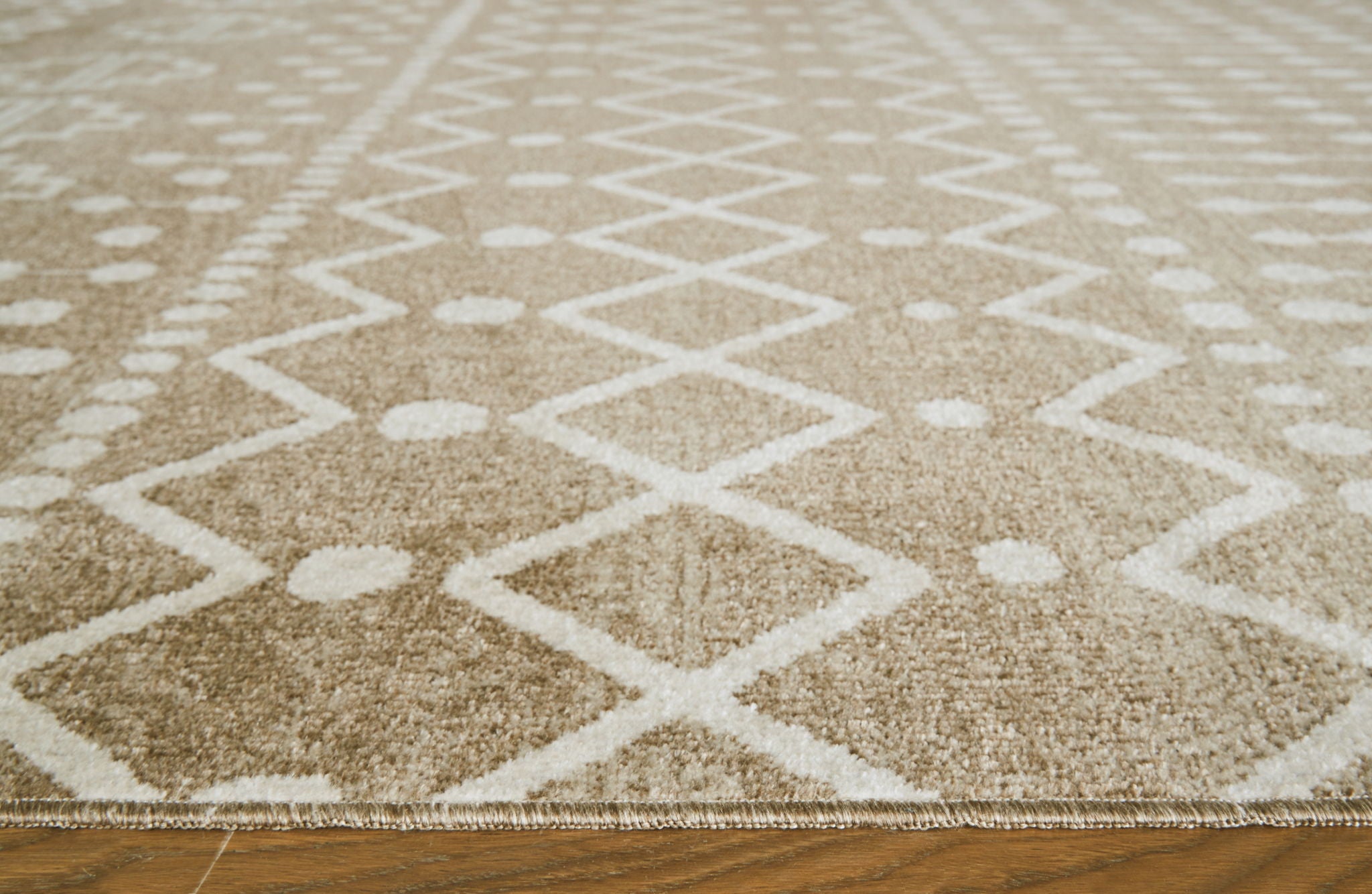 Close-up tan and cream rug pile with diamond and zigzag motif, textured surface