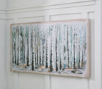 Framed wall art of birch trunks in pale blue, white, and green, mounted on wall