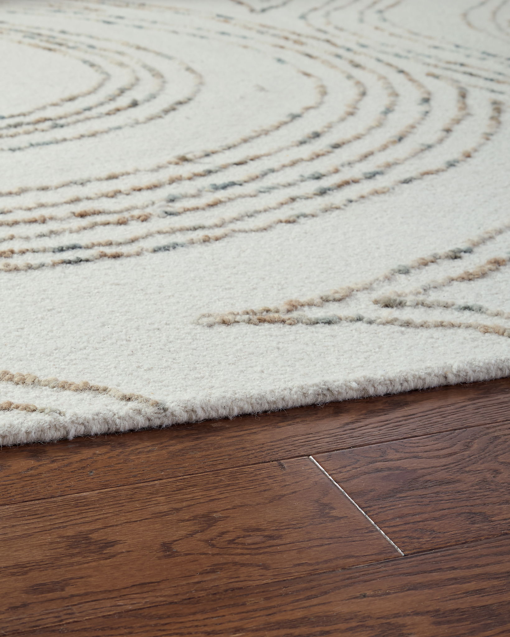 Deenbury rug edge view: off-white pile with beige and gray swirl lines