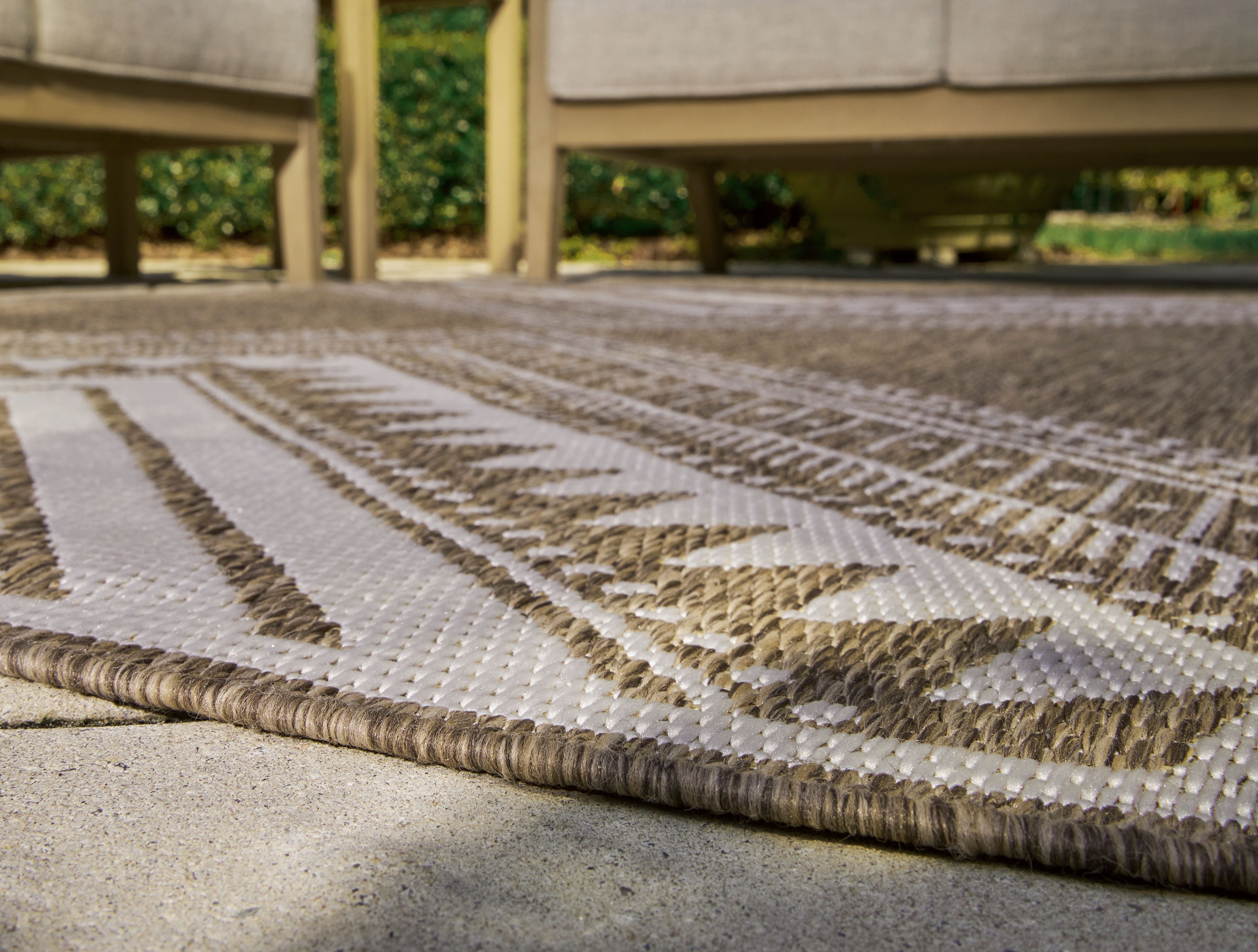 Brown rug with cream diamond and chevron motifs, braided border along edge