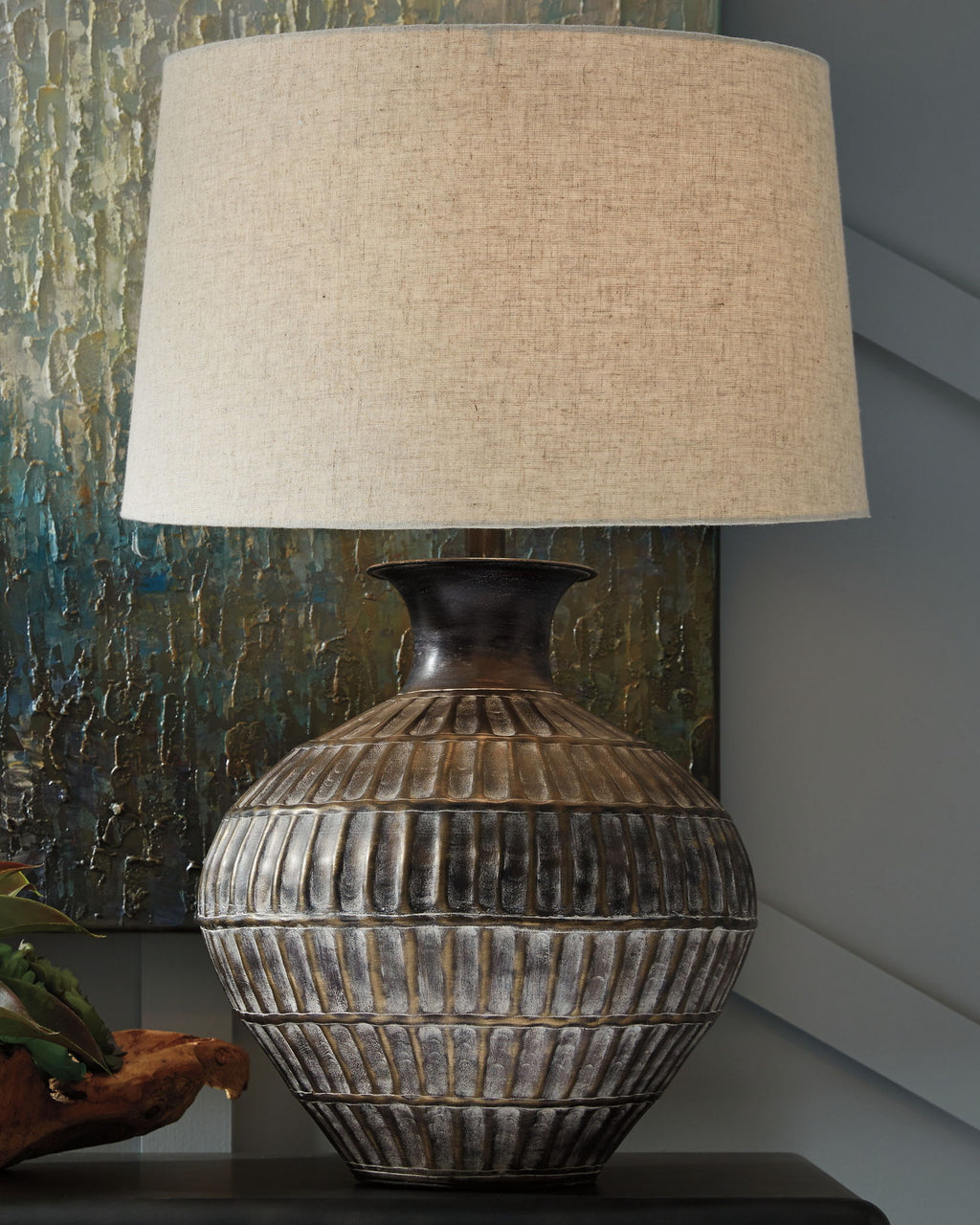 Antique bronze metal table lamp, beige drum shade over ribbed textured urn base.