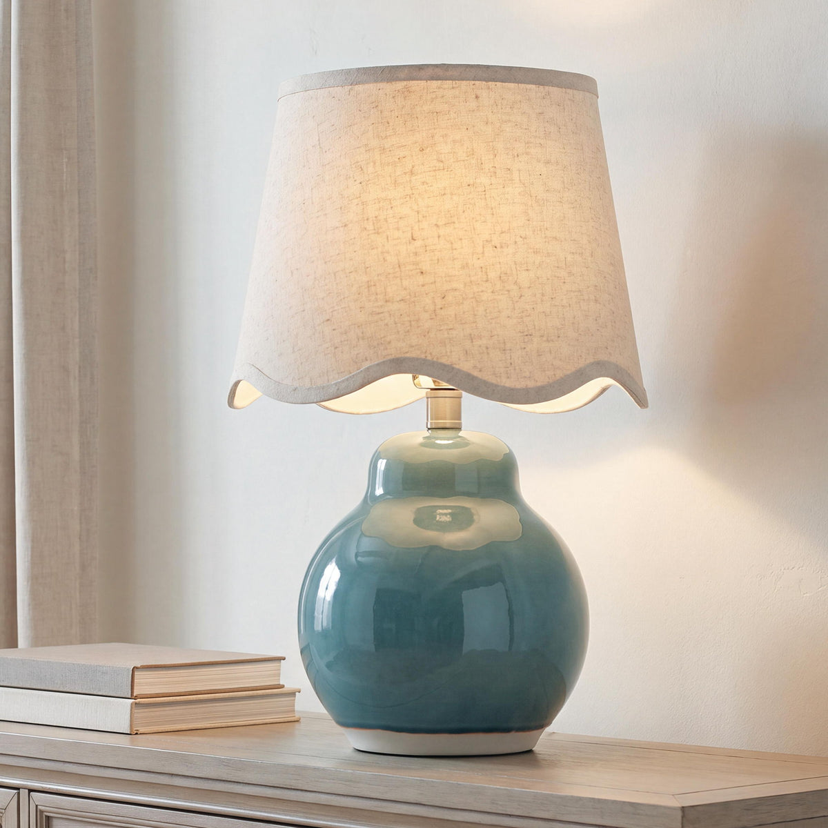 Glowing blue ceramic table lamp with beige fabric drum shade on a side table