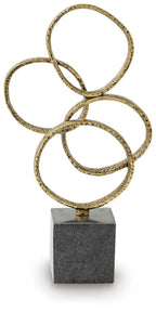 Gold-finish metal ring sculpture on dark stone pedestal, three stacked loops