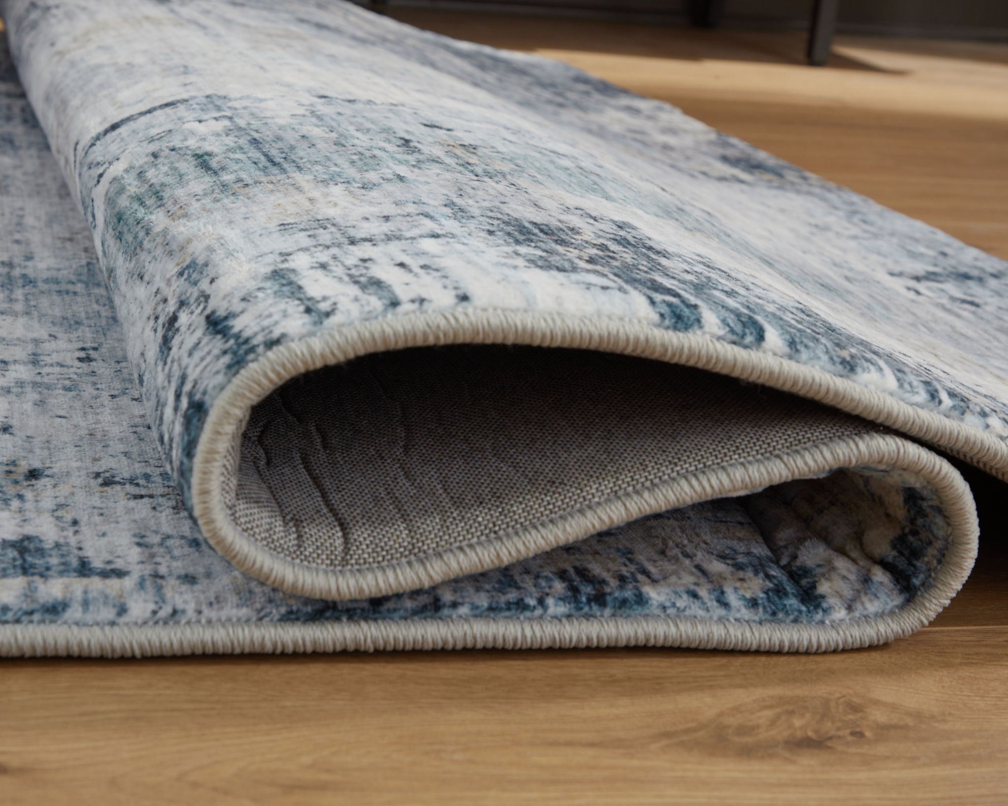 Rolled blue and white abstract rug showing low pile and beige backing underside