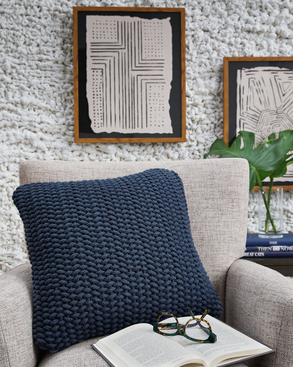 Blue knitted square pillow on a beige sofa with visible chunky textured weave.