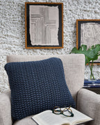 Blue knitted square pillow on a beige sofa with visible chunky textured weave.
