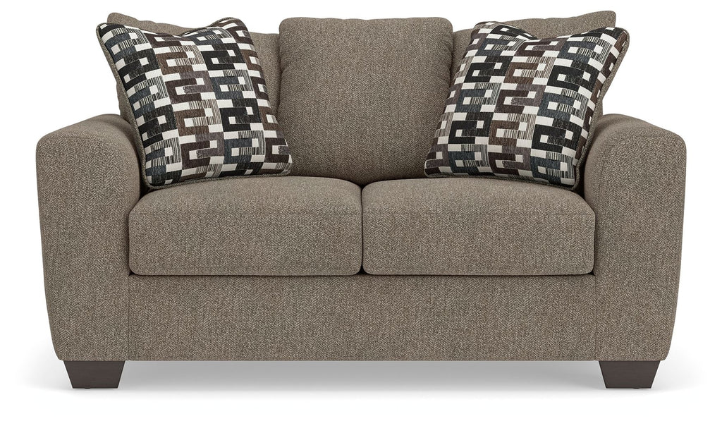 Grey suede loveseat with two patterned throw pillows and upholstered back cushion