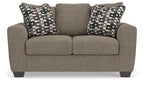 Grey suede loveseat with two patterned throw pillows and upholstered back cushion