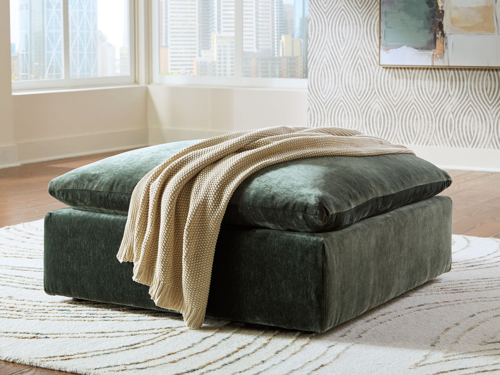 Jade green oversized ottoman with armrest-like sides and folded throw blanket