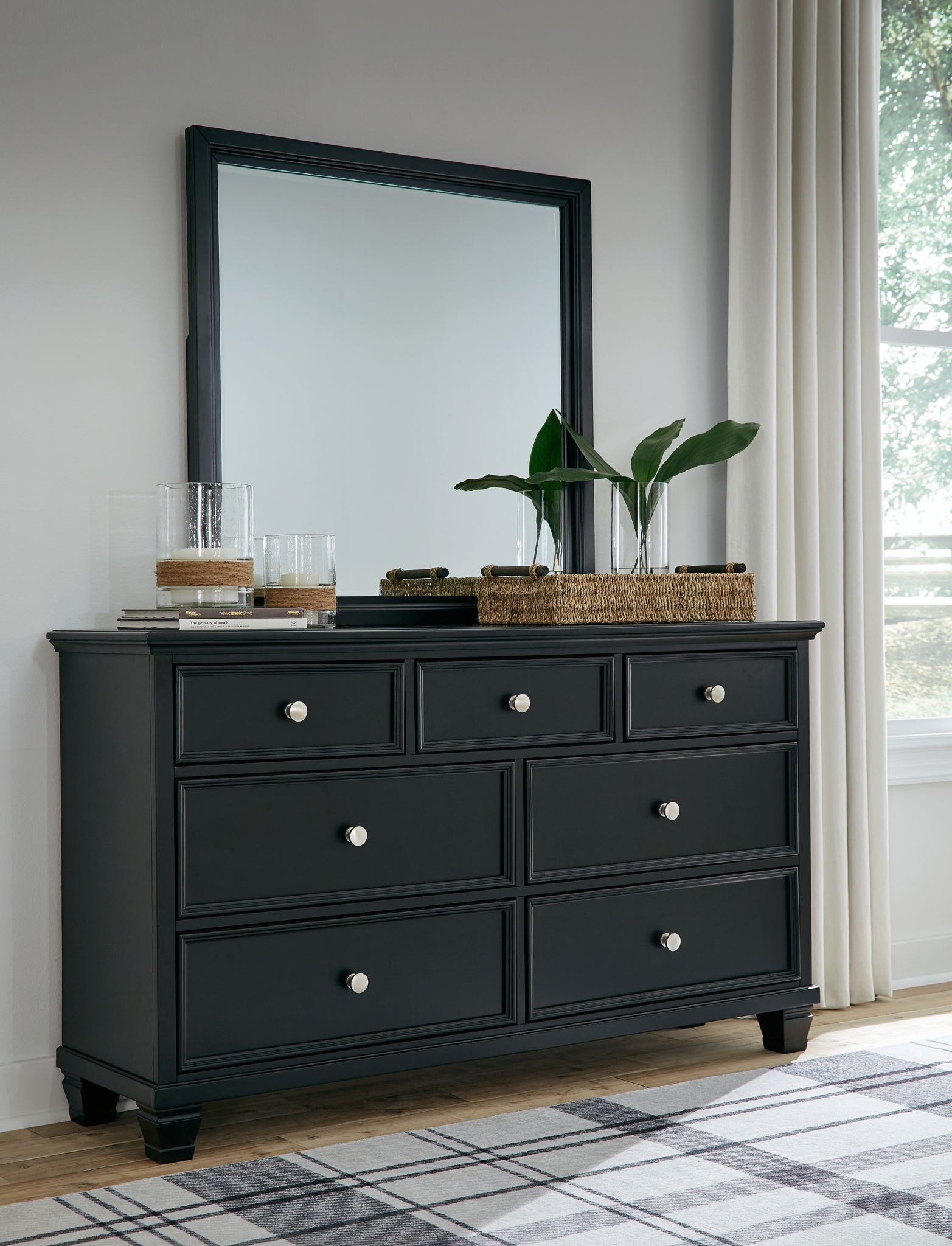 Black dresser with six drawers and round knobs, with a tall wall mirror