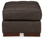Dark brown tufted upholstered ottoman, front view with thick cushioned seat and feet