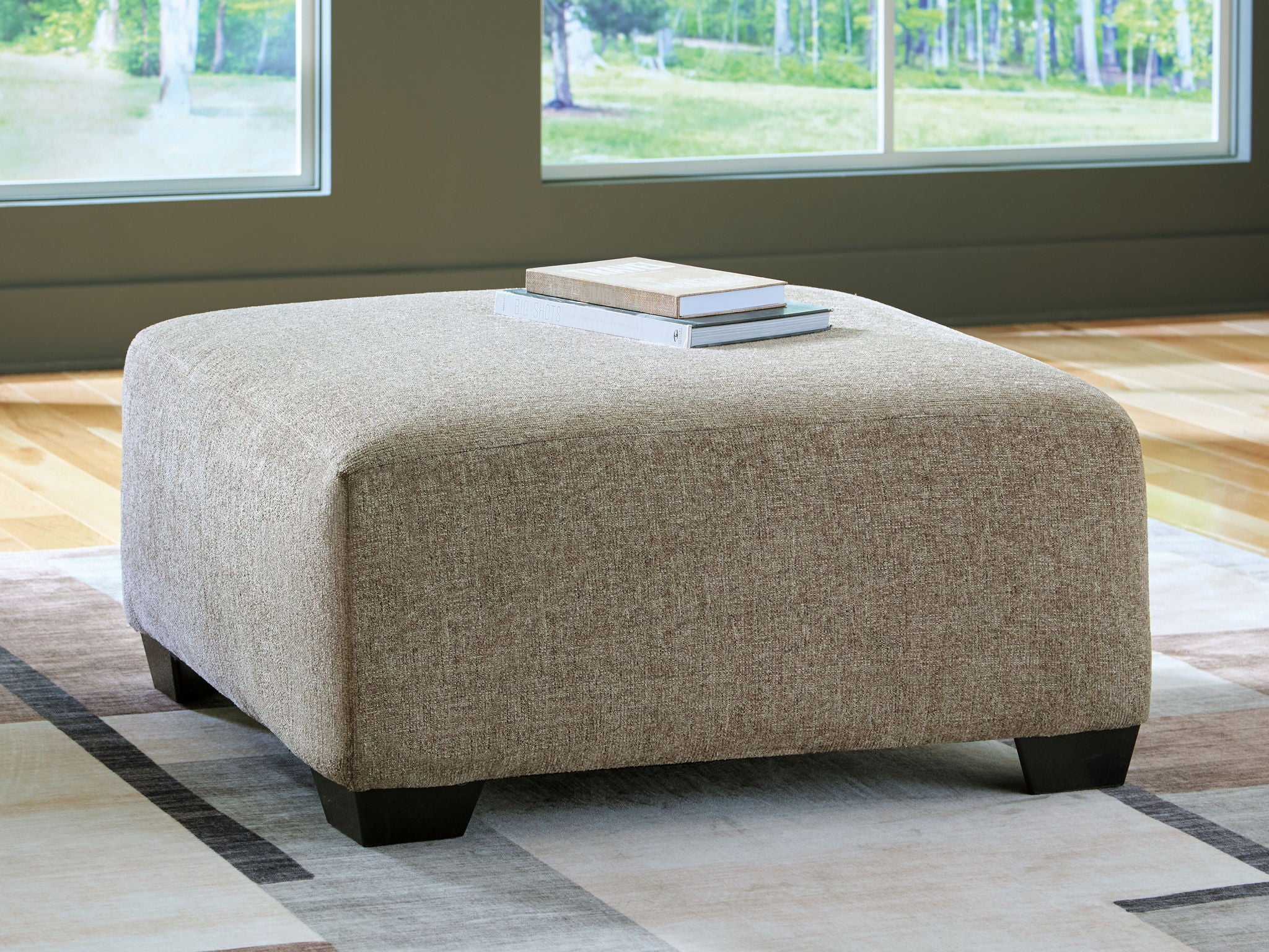 Beige oversized accent ottoman with upholstered seat and low dark legs