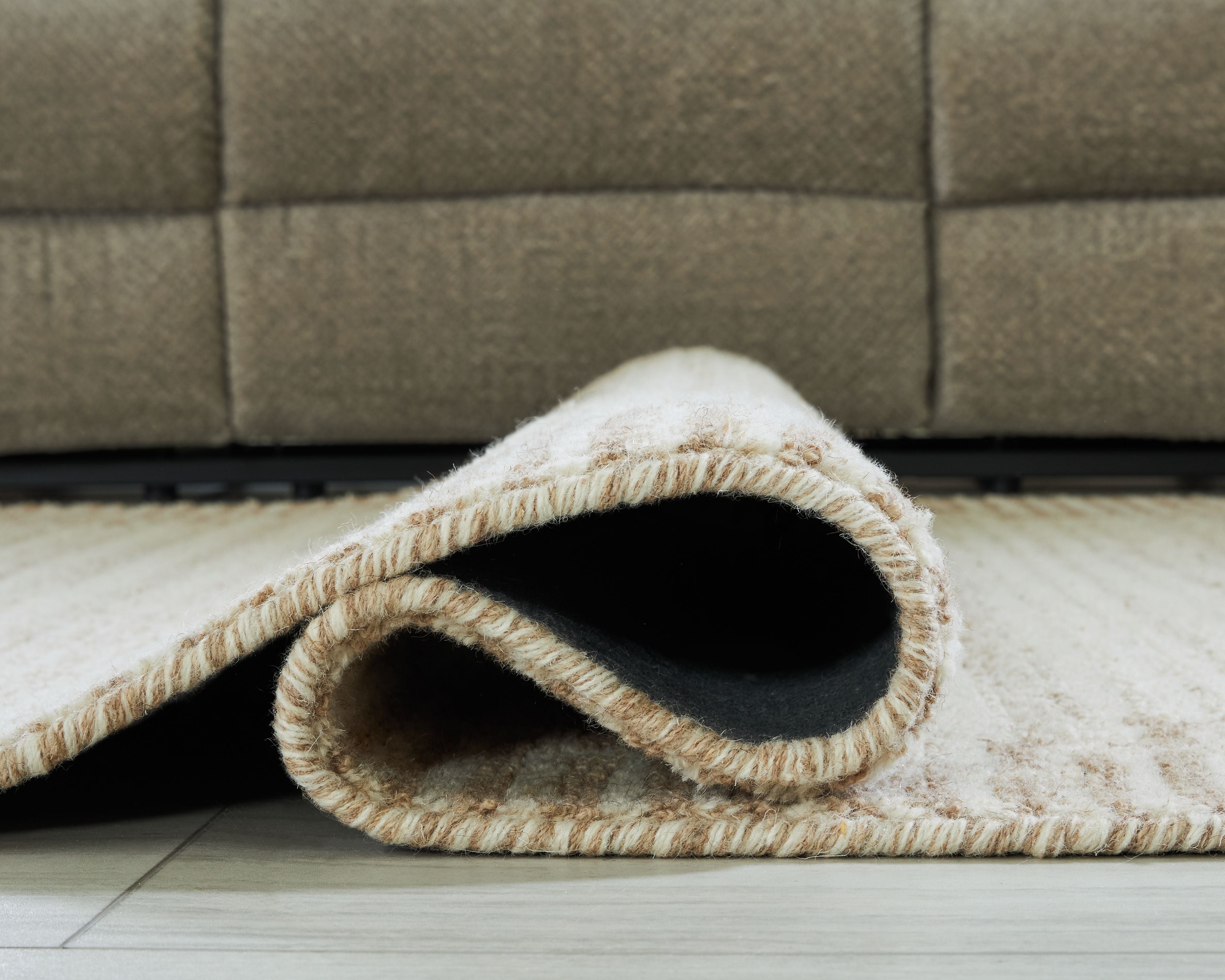 Beige rug showing cut pile texture and stitched edge at folded corner