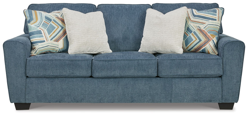 Blue upholstered sofa with three seat cushions and four pillows, two patterned accent throws