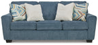 Blue upholstered sofa with three seat cushions and four pillows, two patterned accent throws