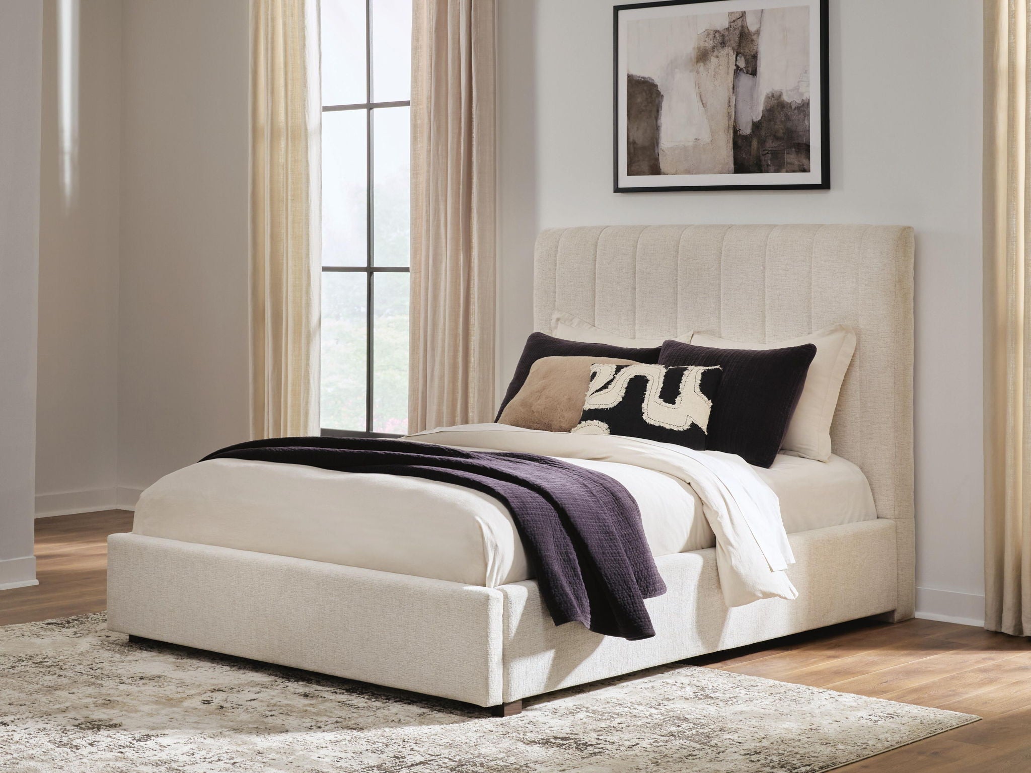 Beige queen upholstered bed with tall channel headboard, neutral bedding, and black throw