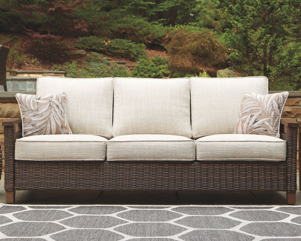 Medium brown wicker sofa with three beige seat sections and patterned throw pillows