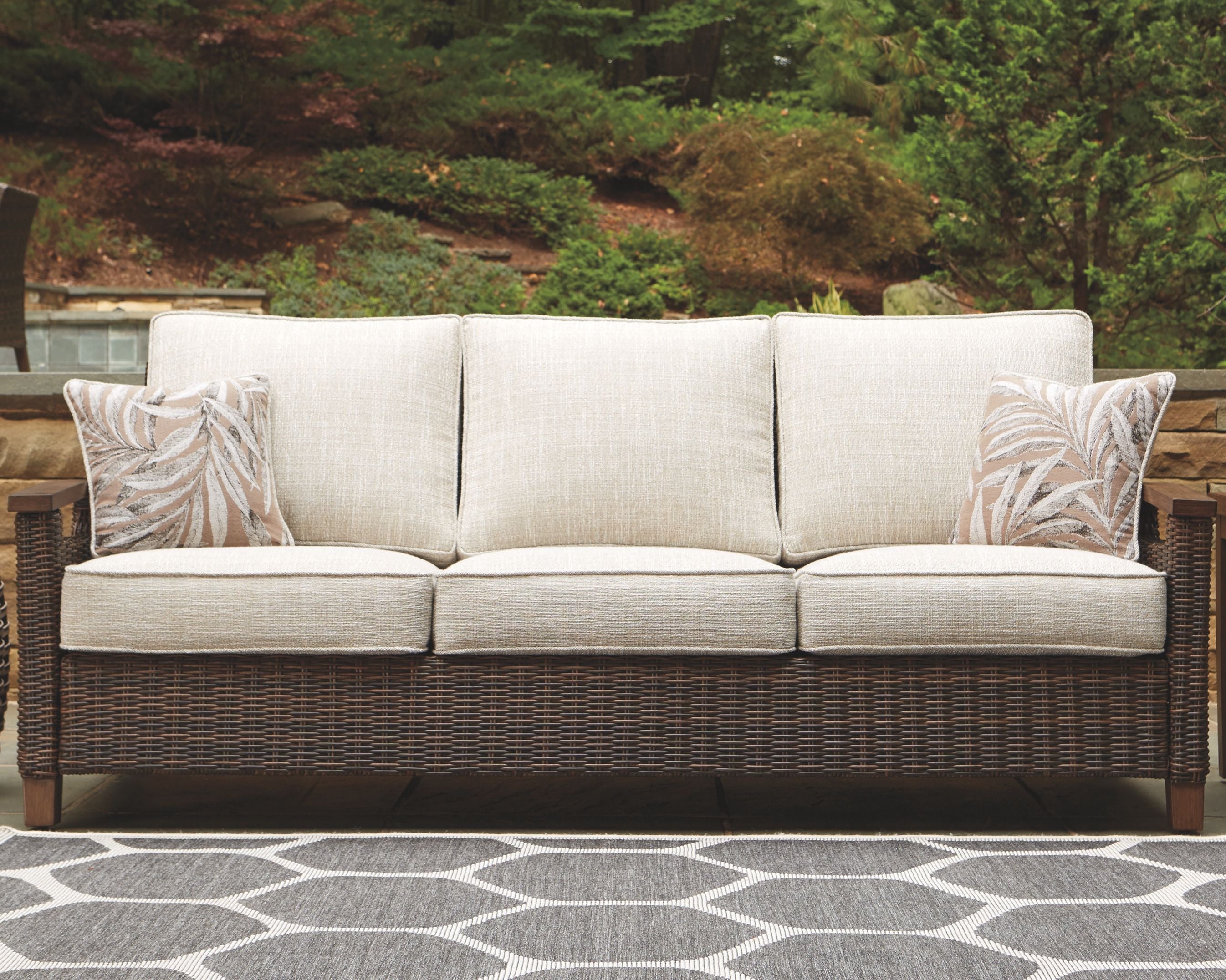 Medium brown wicker sofa with three beige seat sections and patterned throw pillows