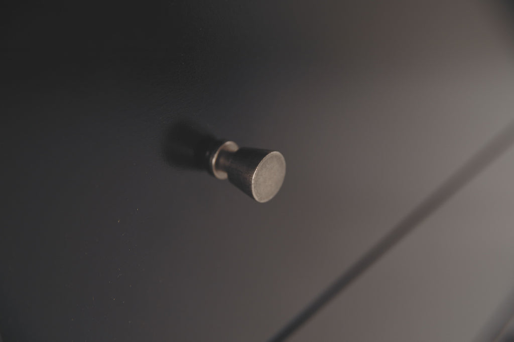 Round metal drawer knob on black dresser drawer front