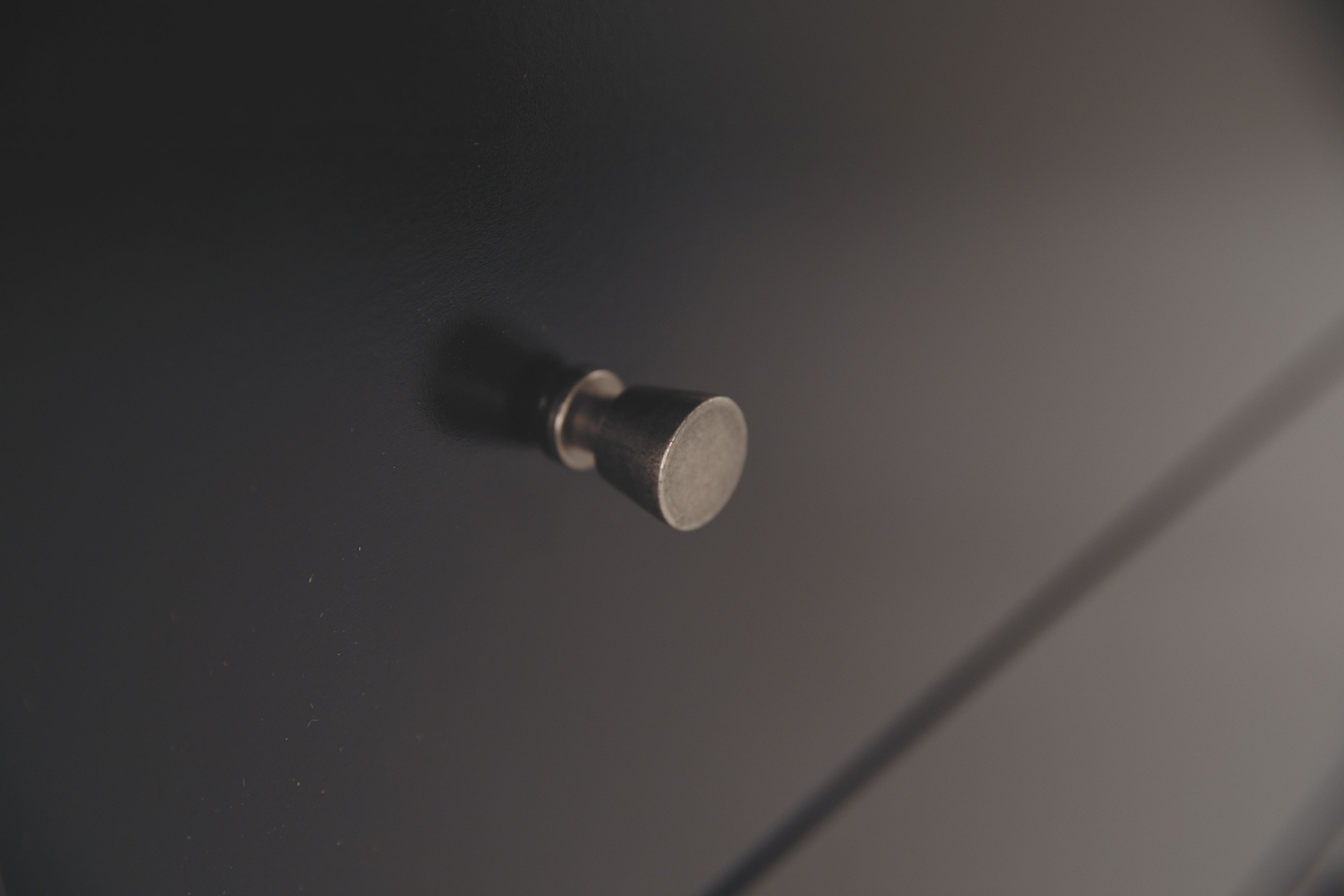 Round metal drawer knob on black dresser drawer front