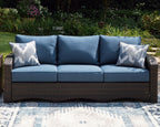 Outdoor sofa with blue cushions and two patterned pillows, brown wicker frame