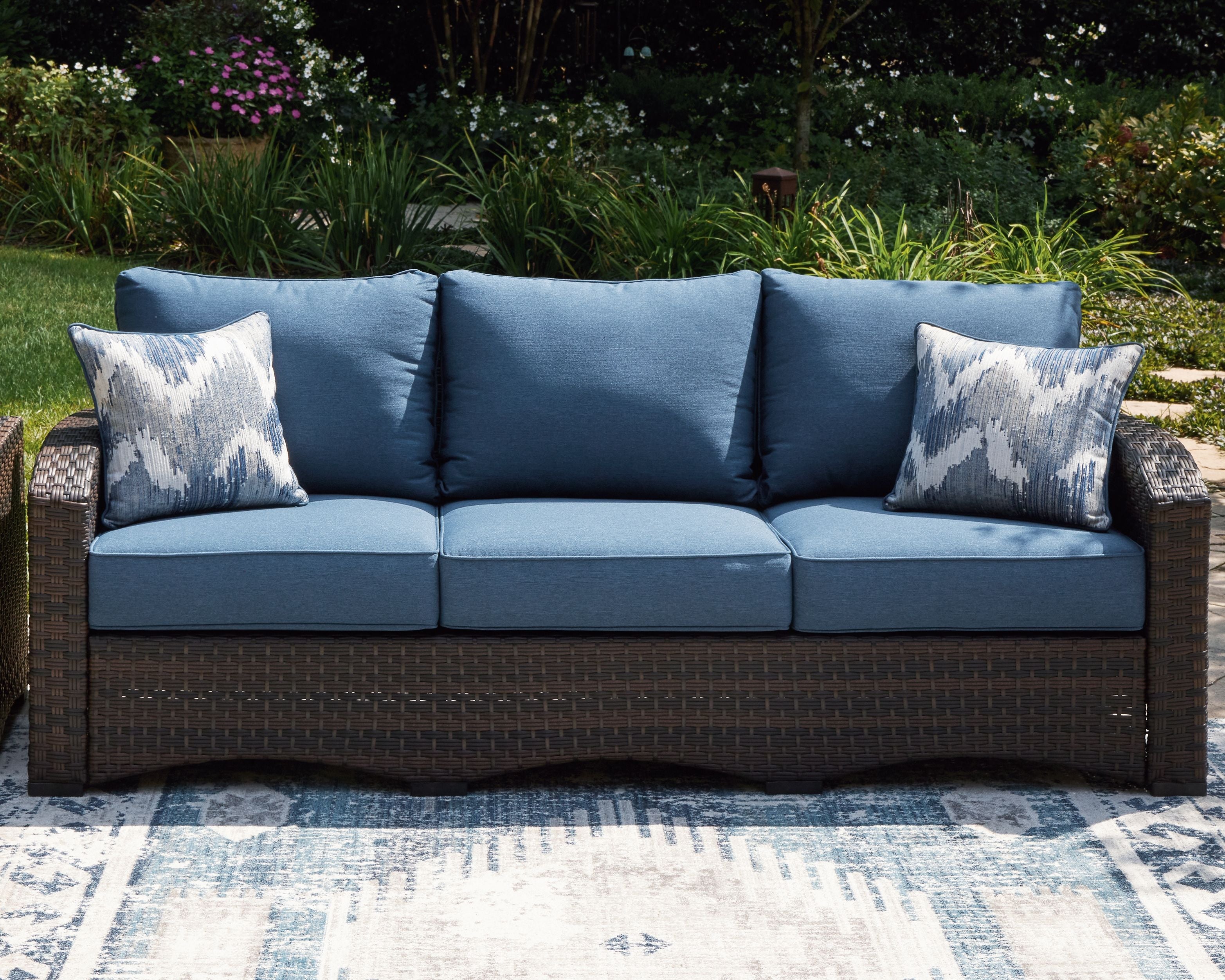 Outdoor sofa with blue cushions and two patterned pillows, brown wicker frame