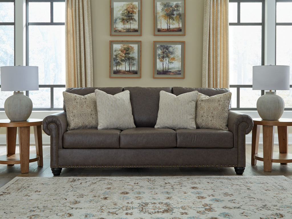 Dark brown sofa with five beige cushions and nailhead trim around frame