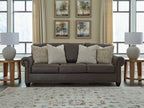 Dark brown sofa with five beige cushions and nailhead trim around frame