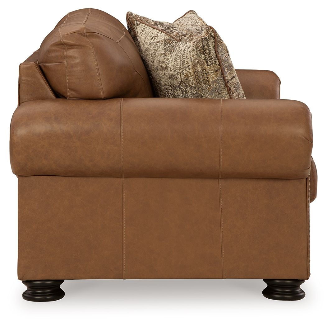 Caramel upholstered loveseat with attached back cushions and two patterned pillows