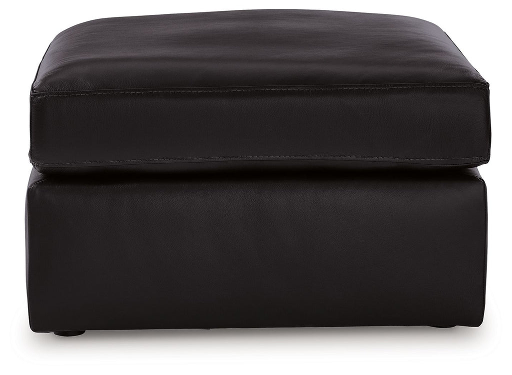 Black upholstered ottoman with rounded top and stitched paneling