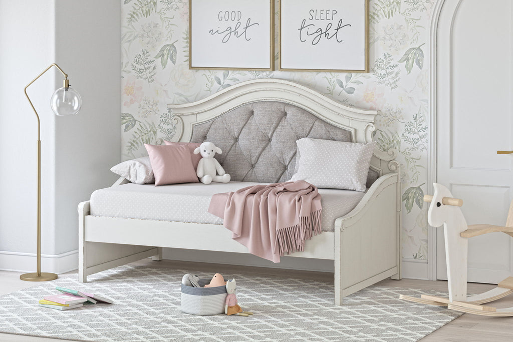 Chipped white twin day bed with tufted gray headboard, pink throw, and decorative pillows