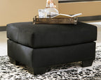 Upholstered ottoman in black fabric, thick padded top with short legs.