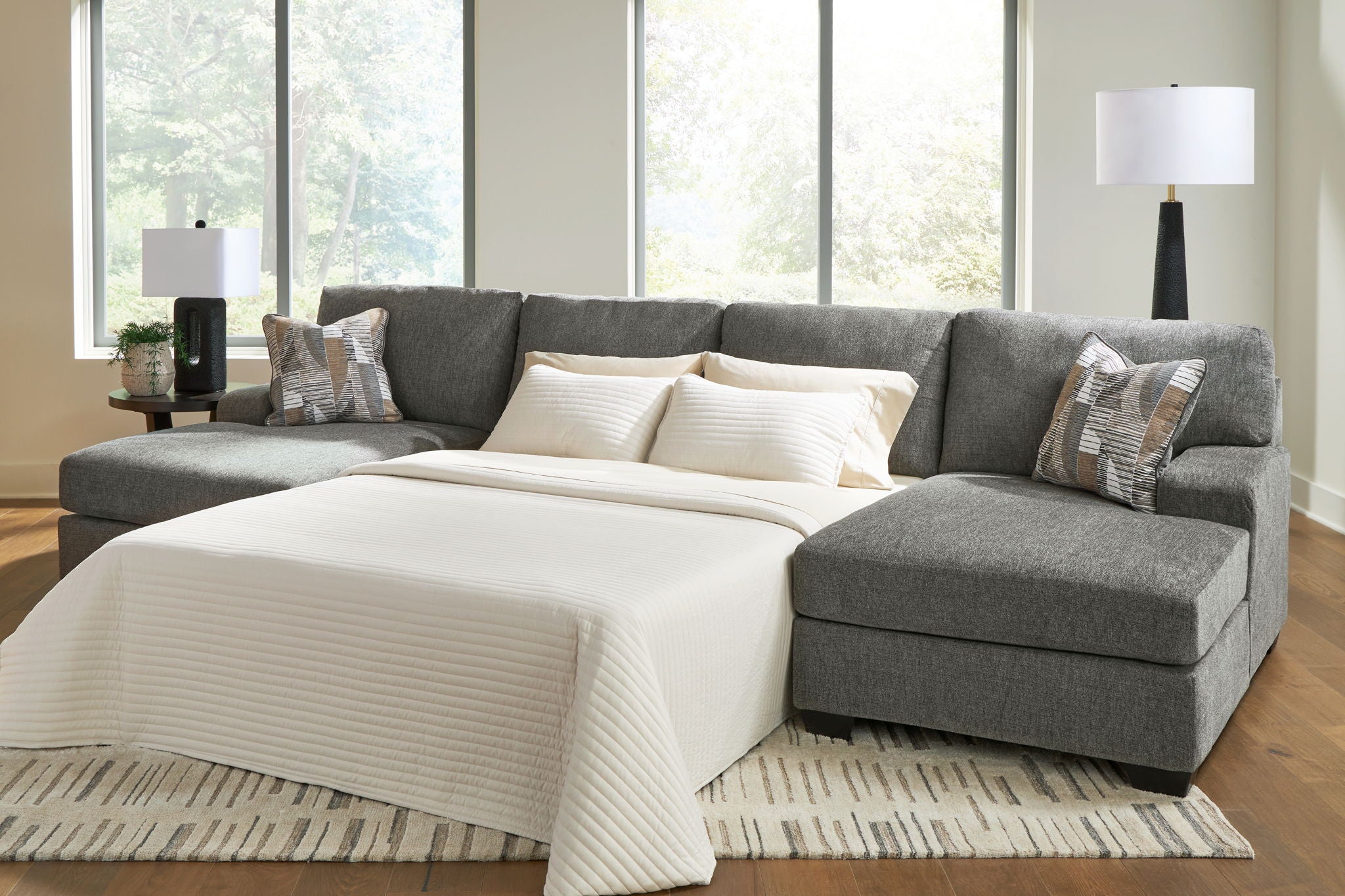 Gray sectional sleeper sofa with chaise, white bedding, and accent pillows